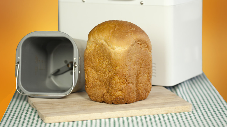 A loaf of bread from a bread machine on a cutting board alongside a bread machine