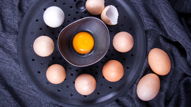 Shelled eggs assembled on egg steamer with one raw cracked egg in the middle of the steamer