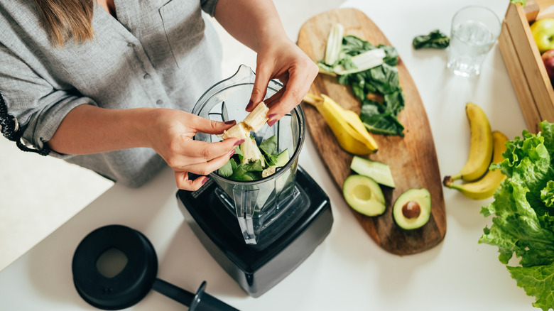 Woman placing banana, spinach, and avocado in a blender from aerial view