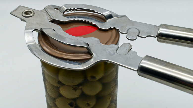 A can of olives being opened by a metal jar opener