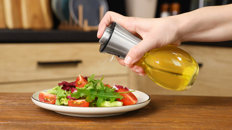 Hand spraying salad on a plate with a glass oil sprayer