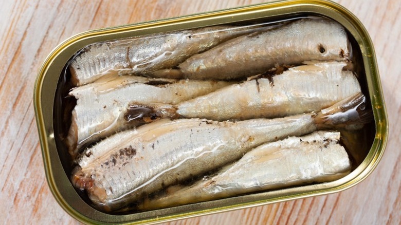a top down view of an open tin of sardines on a wooden table
