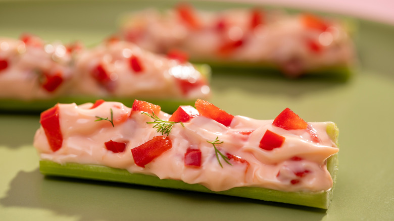 Close up of celery stick stuffed with cream cheese, red peppers, and herbs on green plate