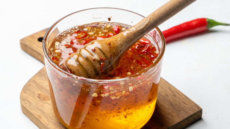 Honey and chili pepper flakes in glass jar on wooden board with honey dipper