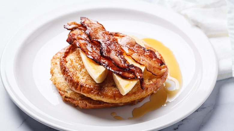 Glazed bacon strips on top of pancakes with butter and syrup on white plate