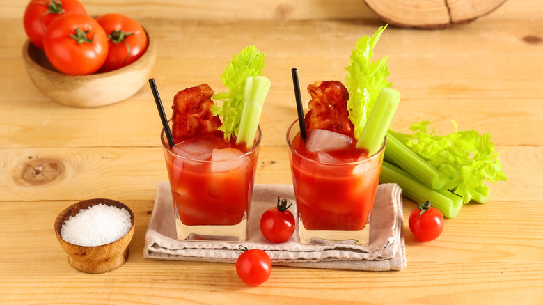 Two bloody marys with bacon, celery, ice cubes, and straws