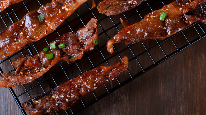 Glazed bacon topped with sesame seeds and green onions on black wire cooling rack