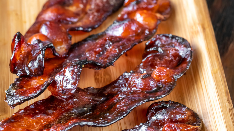 A close-up of glazed bacon strips on a wooden board