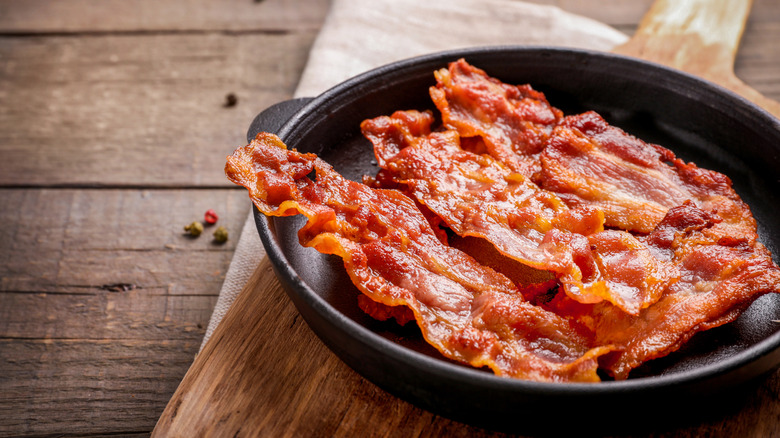 Pieces of cooked bacon in a cast iron pan on a wooden board