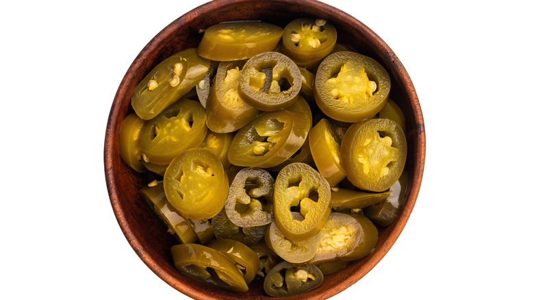 A wooden bowl with pickled jalapeños on white background