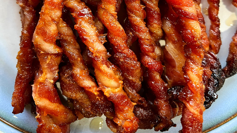 Greasy cooked bacon twists in a pile on white background