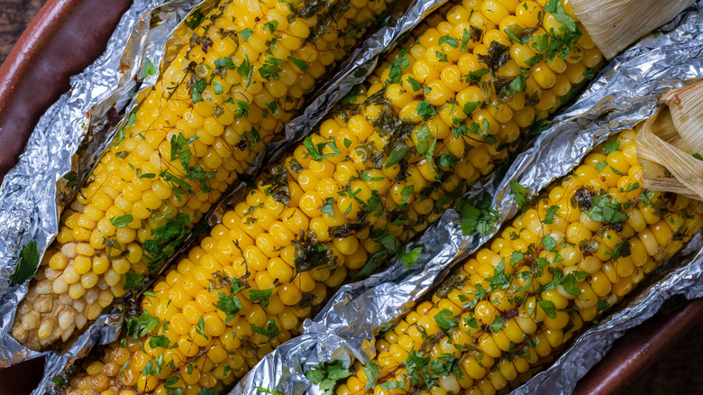 Corn wrapped in foil  topped with herbs
