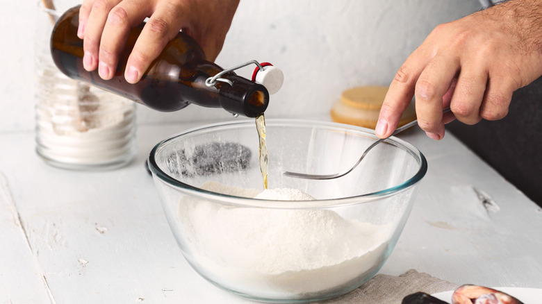 A person's hand pouring beer into a bowl from a brown bottle