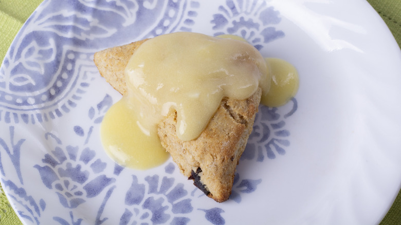 A scone topped with lemon curd on a blue and white plate