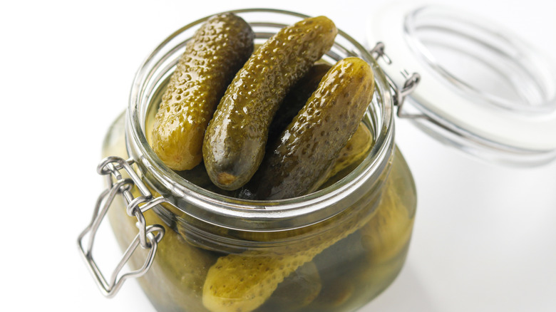 Jar with pickles submerged in brine, showing whole cucumbers and glossy texture, isolated on a clean white background.