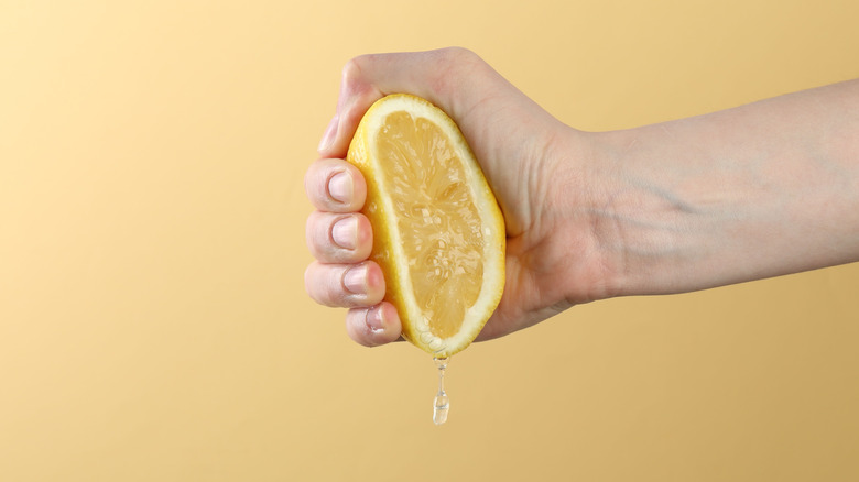 Hand squeezing lemon half on yellow background, closeup