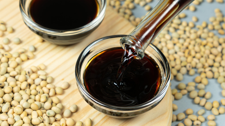 Stream of soy sauce pouring from long-stemmed glass jar and filling a small sauce dish.
