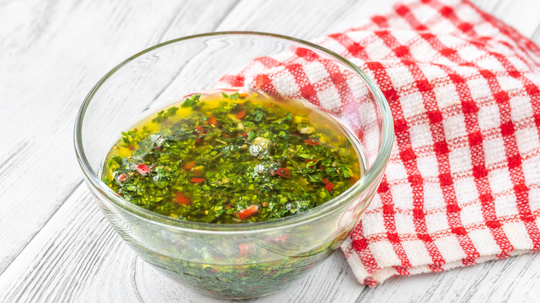 A glass bowl of chimichurri sauce on a wood table