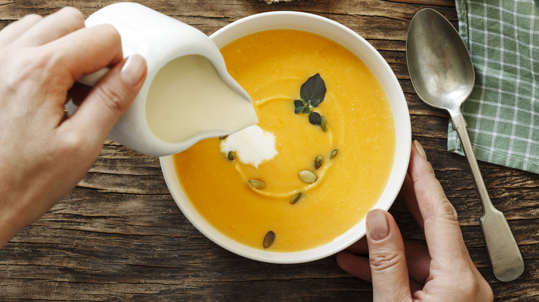 Person pouring cream into pumpkin soup