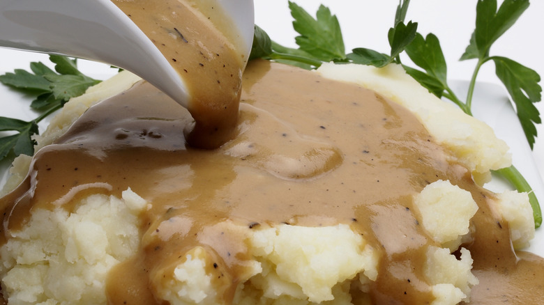 Close up of gravy boat pouring over mashed potatoes