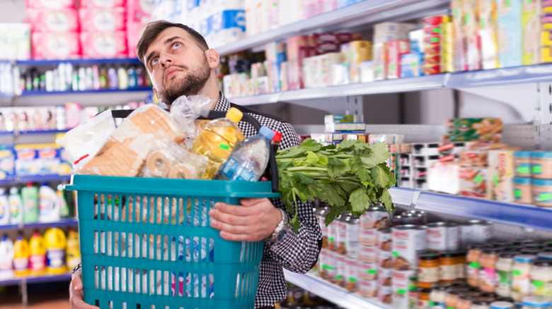 A man with arms full of more groceries than he needs as he thinks