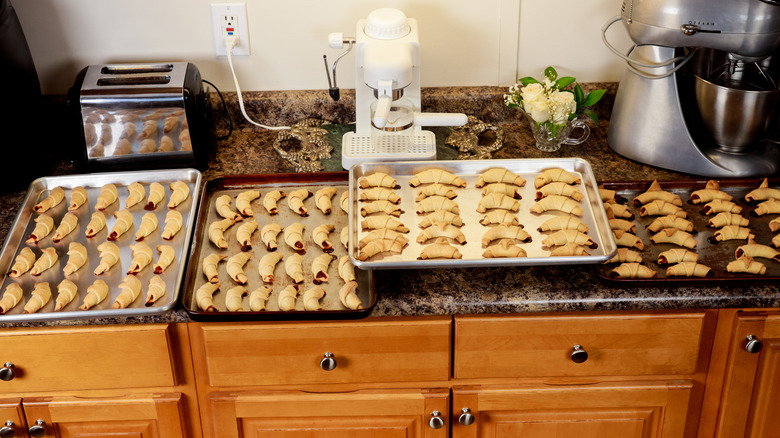 A kitchen counter completely overrun by trays of cooked croissants