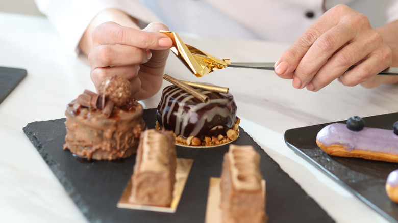 A baker putting edible gold on an elaborately decorated pastry