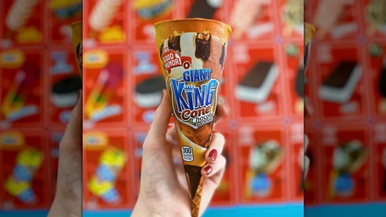 A hand holding a Giant King Cone in front of a red display