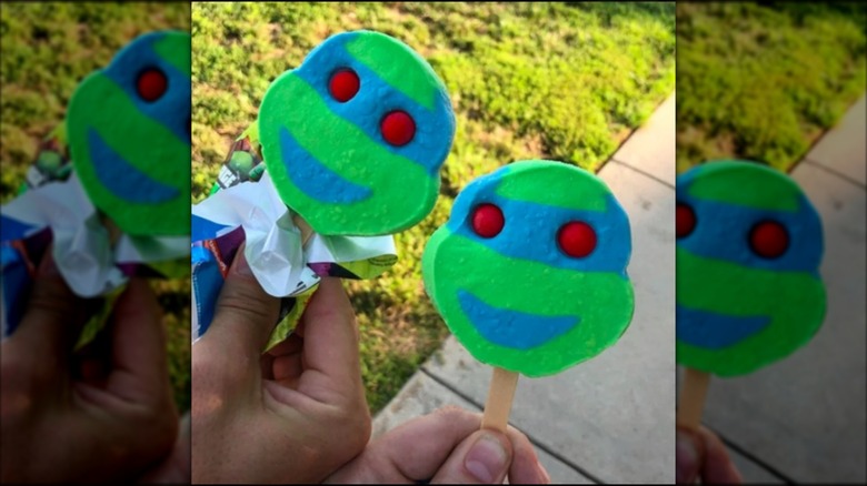 Someone holding two Teenage Mutant Ninja Turtle ice cream bars outside, mirrored