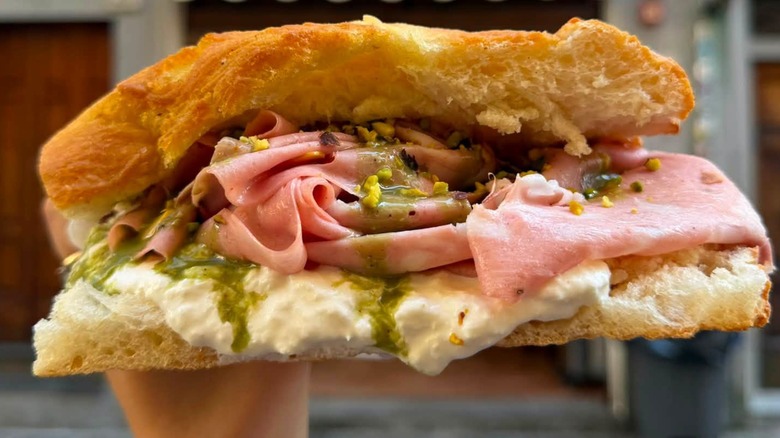 Hand holding a ham sandwich with pesto sauce and soft cheese.