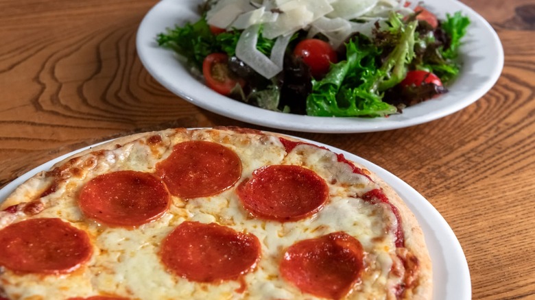 Pizza and a bowl of salad on a wooden table.