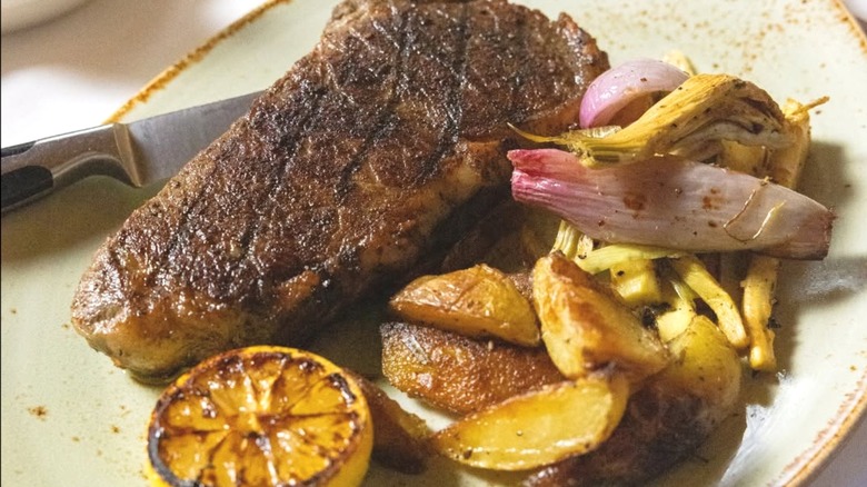 Steak, potatoes, and onion on white plate.