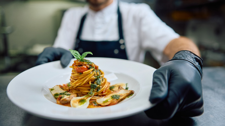 A black-gloved chef arranging a plate of pasta.