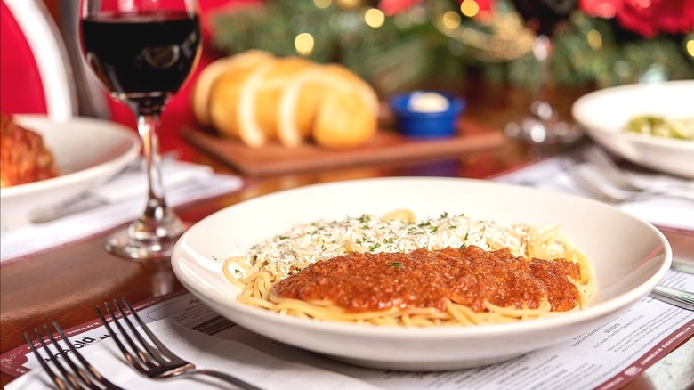 Cutlery, a glass of wine, and a bowl of pasta arranged on a table.