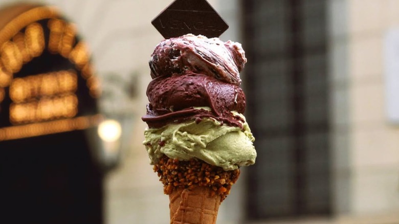 Three scoops of colorful ice cream on a cone crusted with nuts.