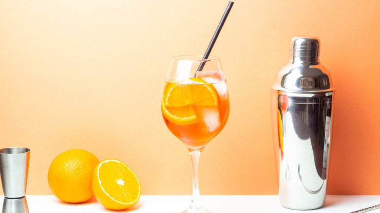 Aperol spritz on a white surface with orange slices and a shaker
