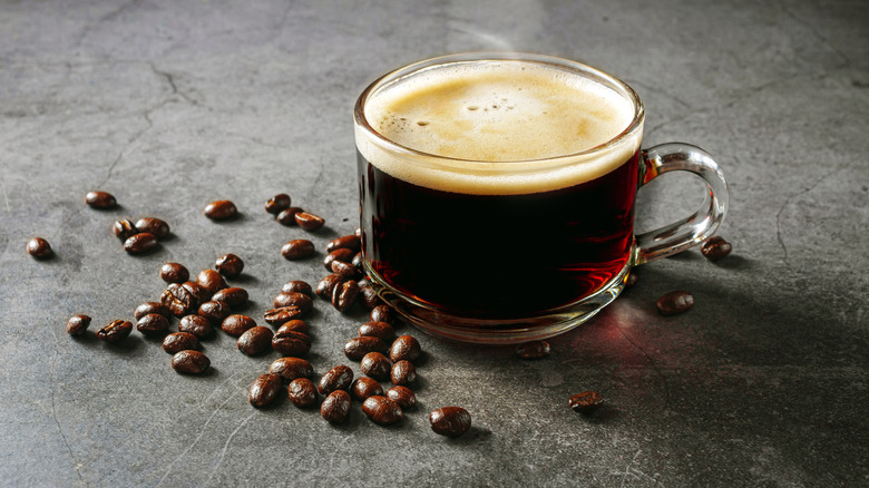 coffee in a glass mug beside pile of coffee beans