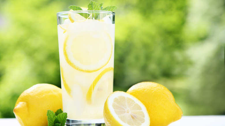 glass of lemonade with green garnish set outdoors with lemons