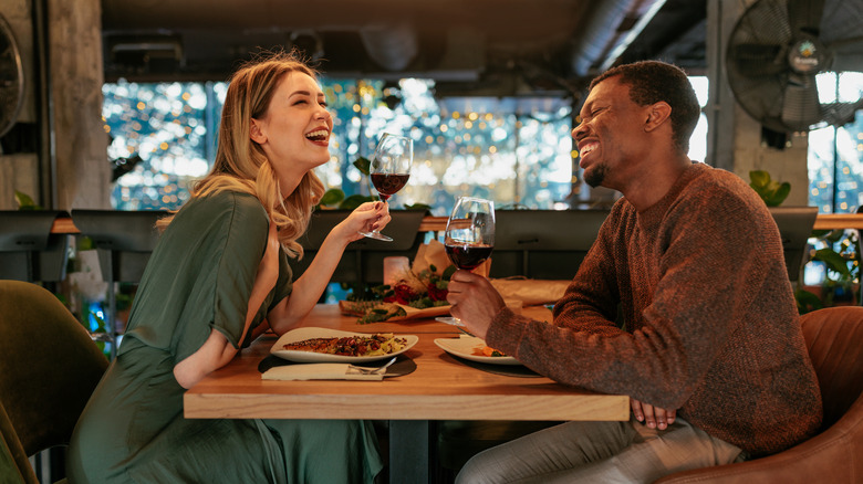 A couple is smiling and talking while enjoying wine and food in a restaurant