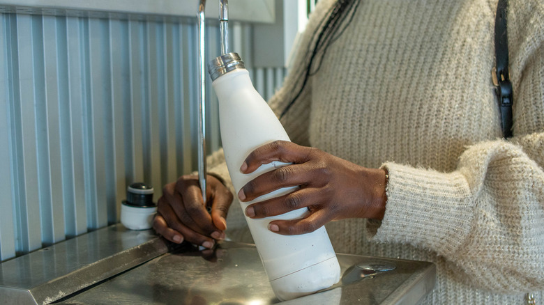 A woman filling her reusable bottle at an airport fountain