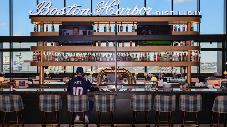 A man in a sports jersey sitting at the Boston Harbor Distillery Bar inside Logan International Airport