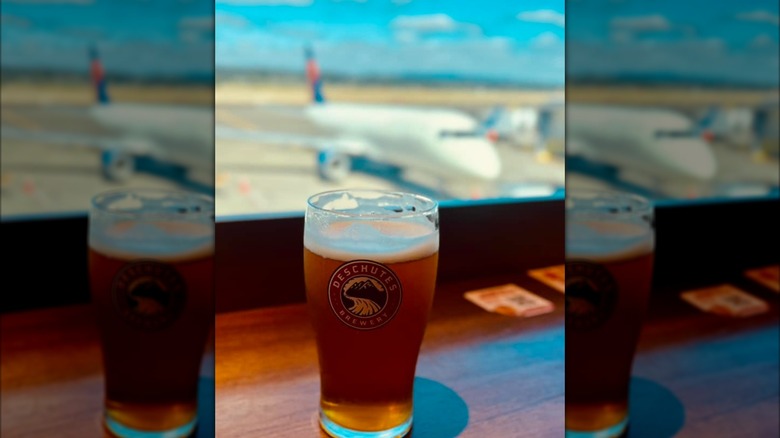A draft beer perched in front of a window showing an airplane