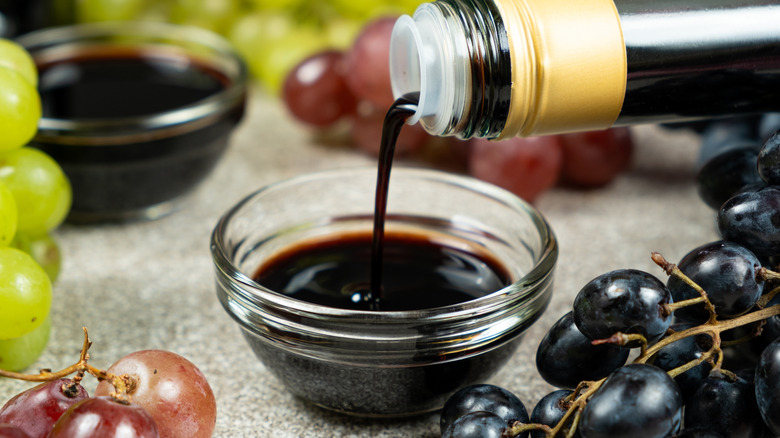 Bottle of balsamic vinegar being poured into a glass bowl surrounded by grapes