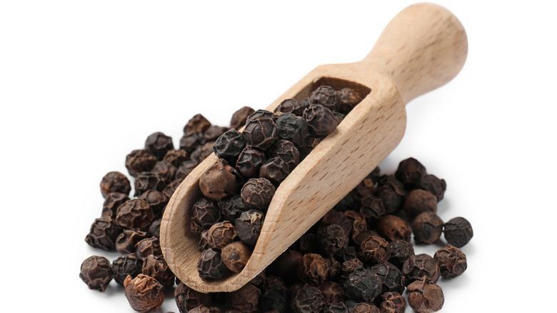 A pile of black peppercorns and a wooden scoop