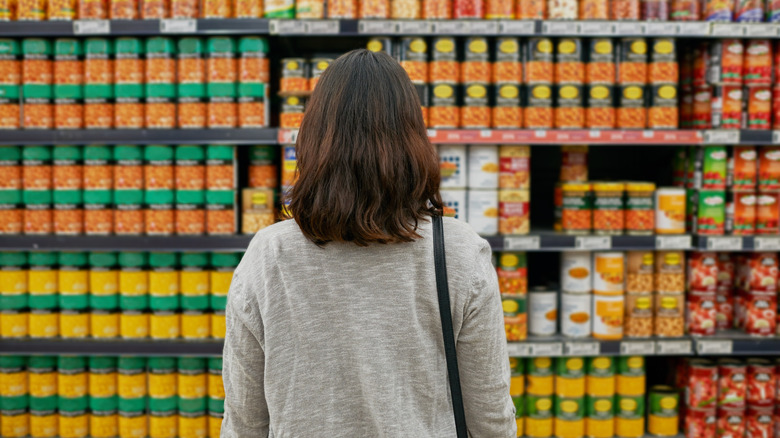 A woman looking at shelves of canned food in a supermarket