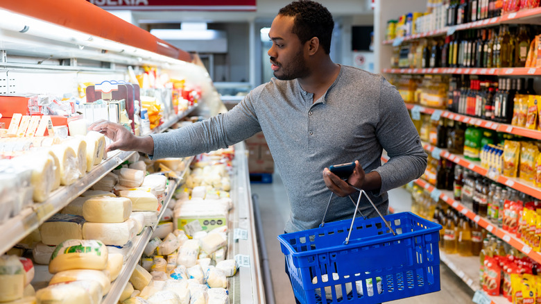A man in a supermarket reaching for a block of cheese from the cooler display