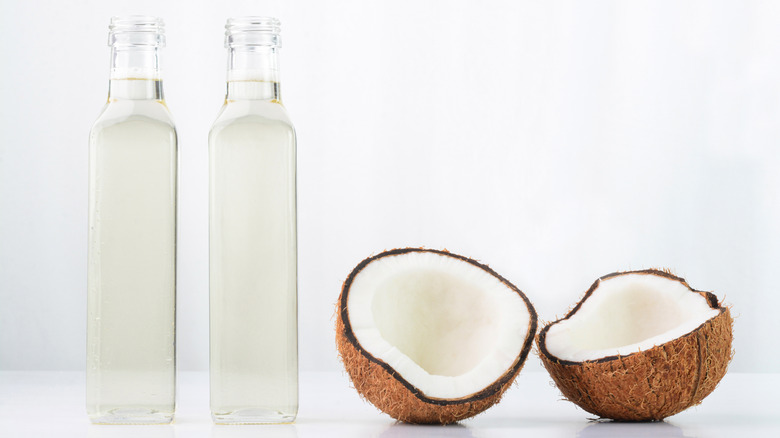 Two bottles of coconut oil next to two coconut halves