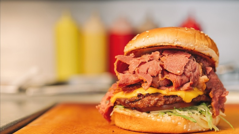 A cheeseburger topped with pastrami resting on a counter.