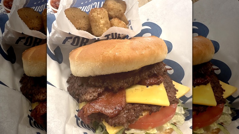 A sleeve of cheese curds leaning on a double bacon cheeseburger from Culver's.