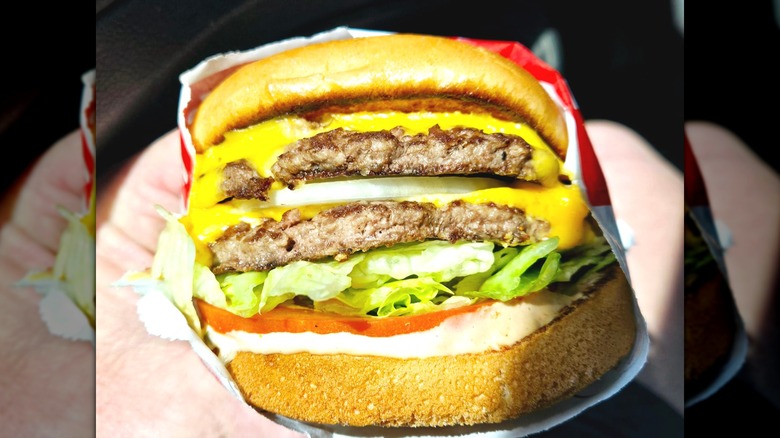 Two hands holding an In-N-Out double cheeseburger with onion, lettuce, tomato, and mayo.